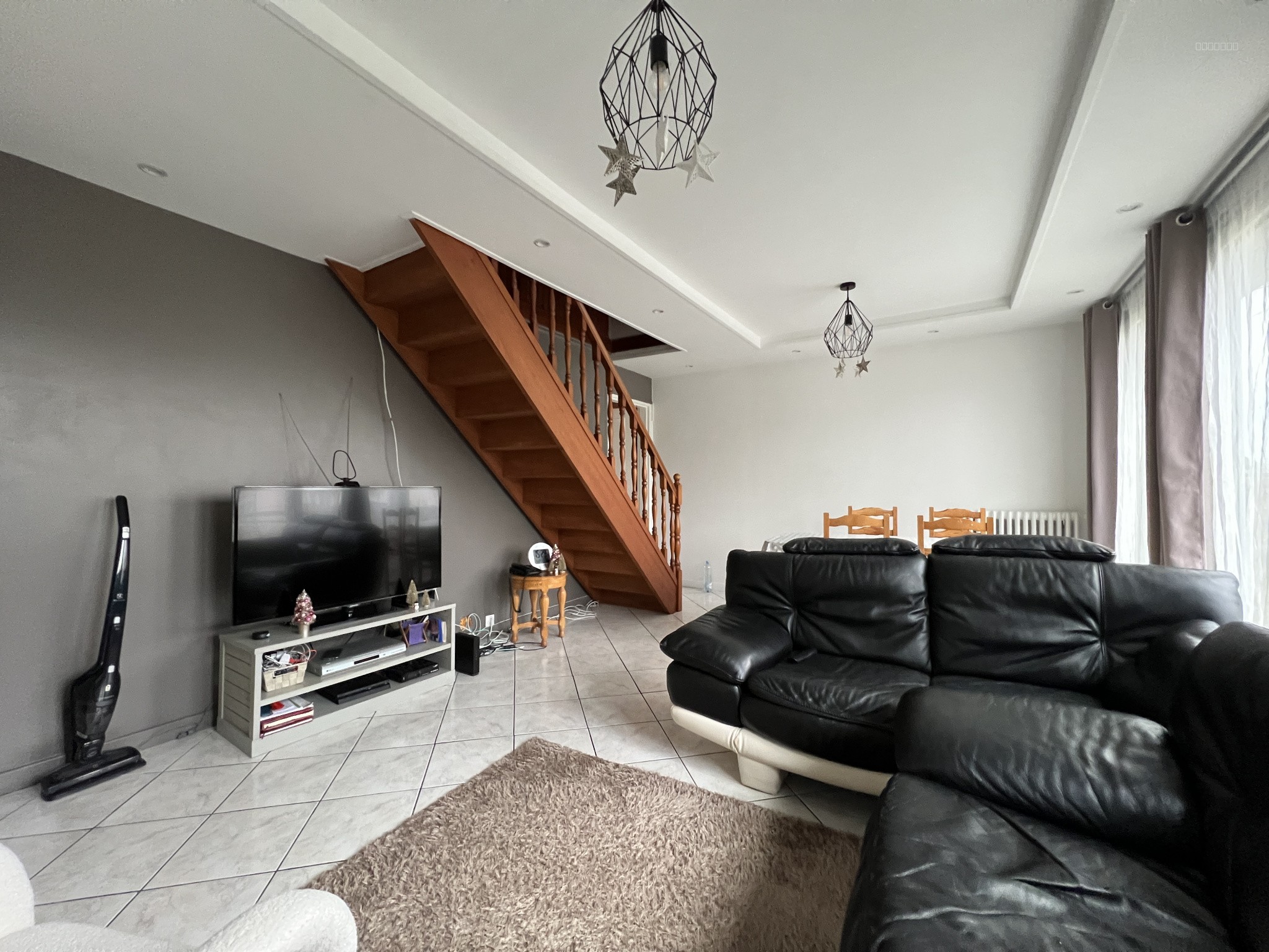 Maison à vendre à Louvres : salon avec canapé noir, escalier bois et carrelage