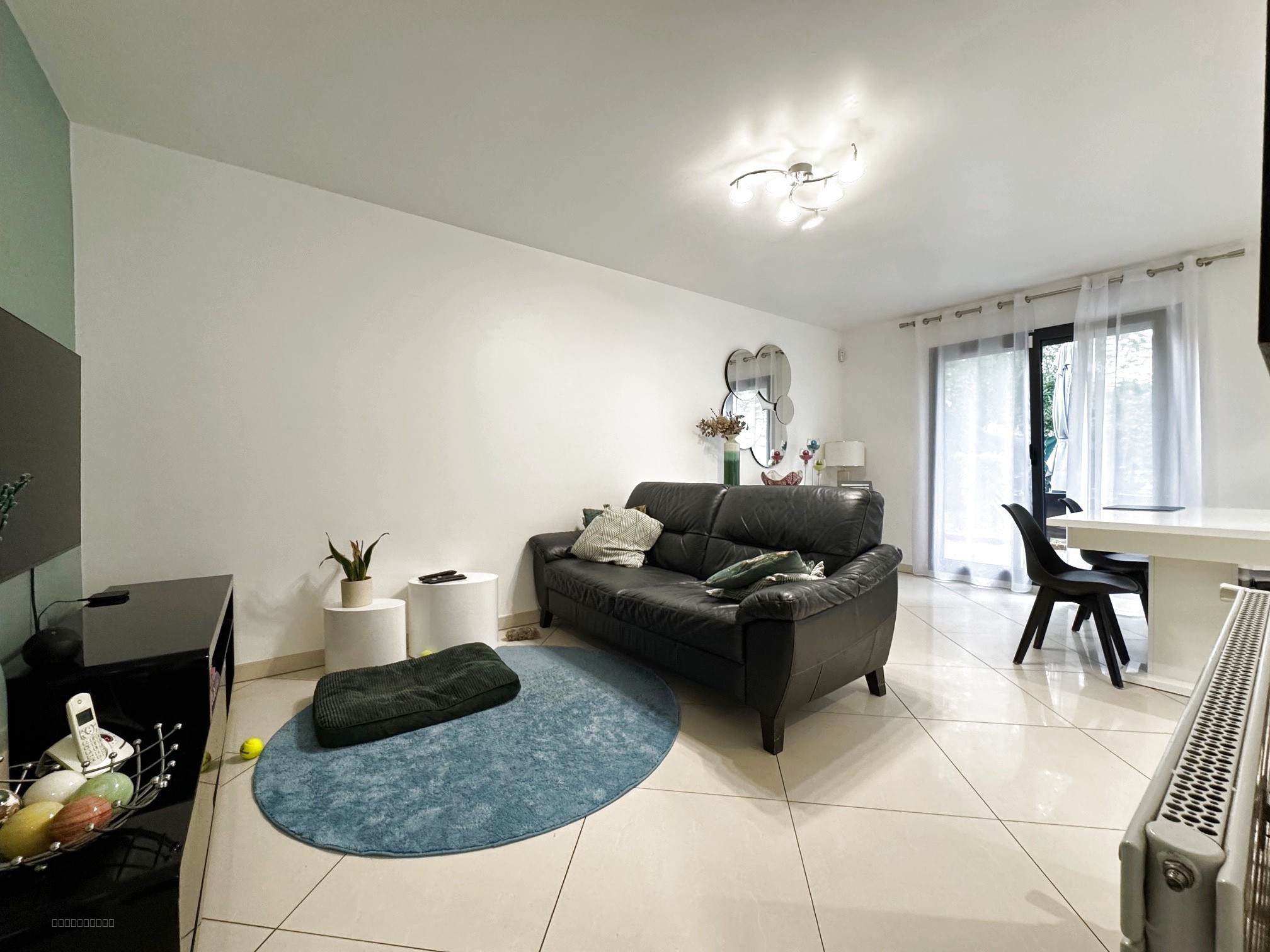Maison à vendre à Louvres : salon avec canapé noir, tapis bleu et table blanche