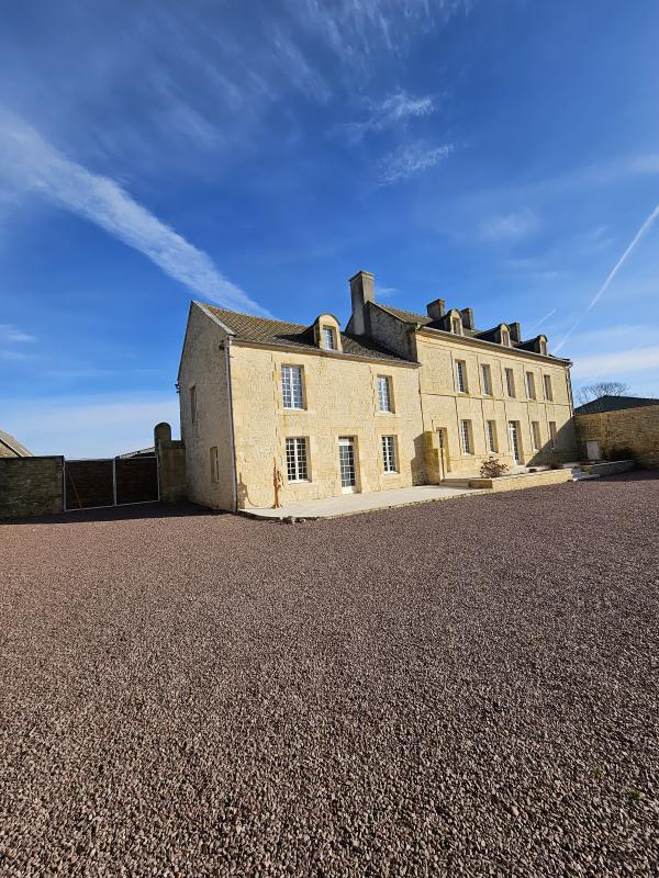 Maison à vendre à Putot-en-Bessin : façade d'une maison en pierre avec plusieurs fenêtres et un toit mansardé