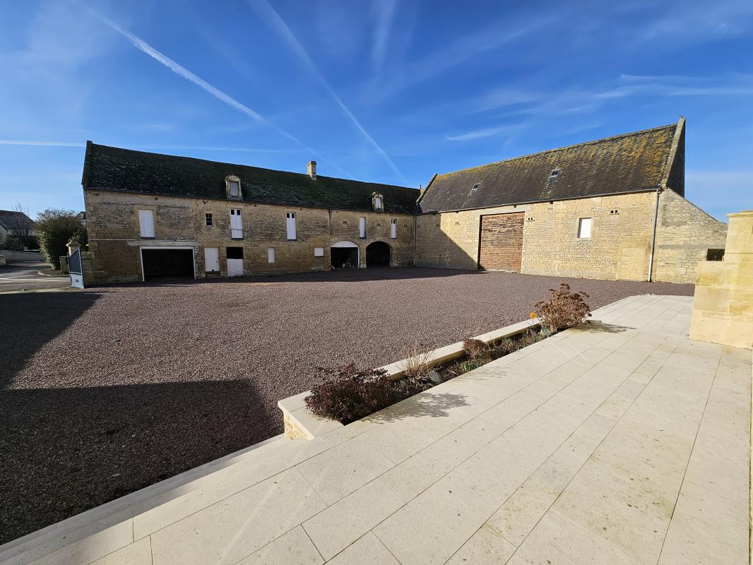 Maison à vendre à Putot-en-Bessin : cour pavée avec une terrasse en pierre et des dépendances en pierre