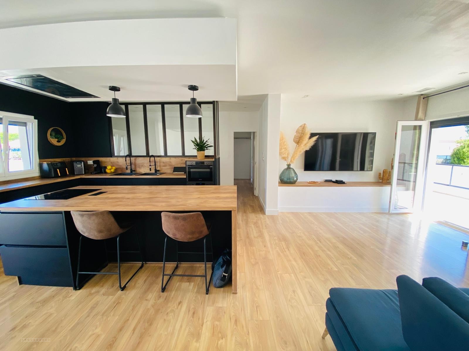 Villa à vendre à Bompas : cuisine noire avec îlot en bois et salon adjacent