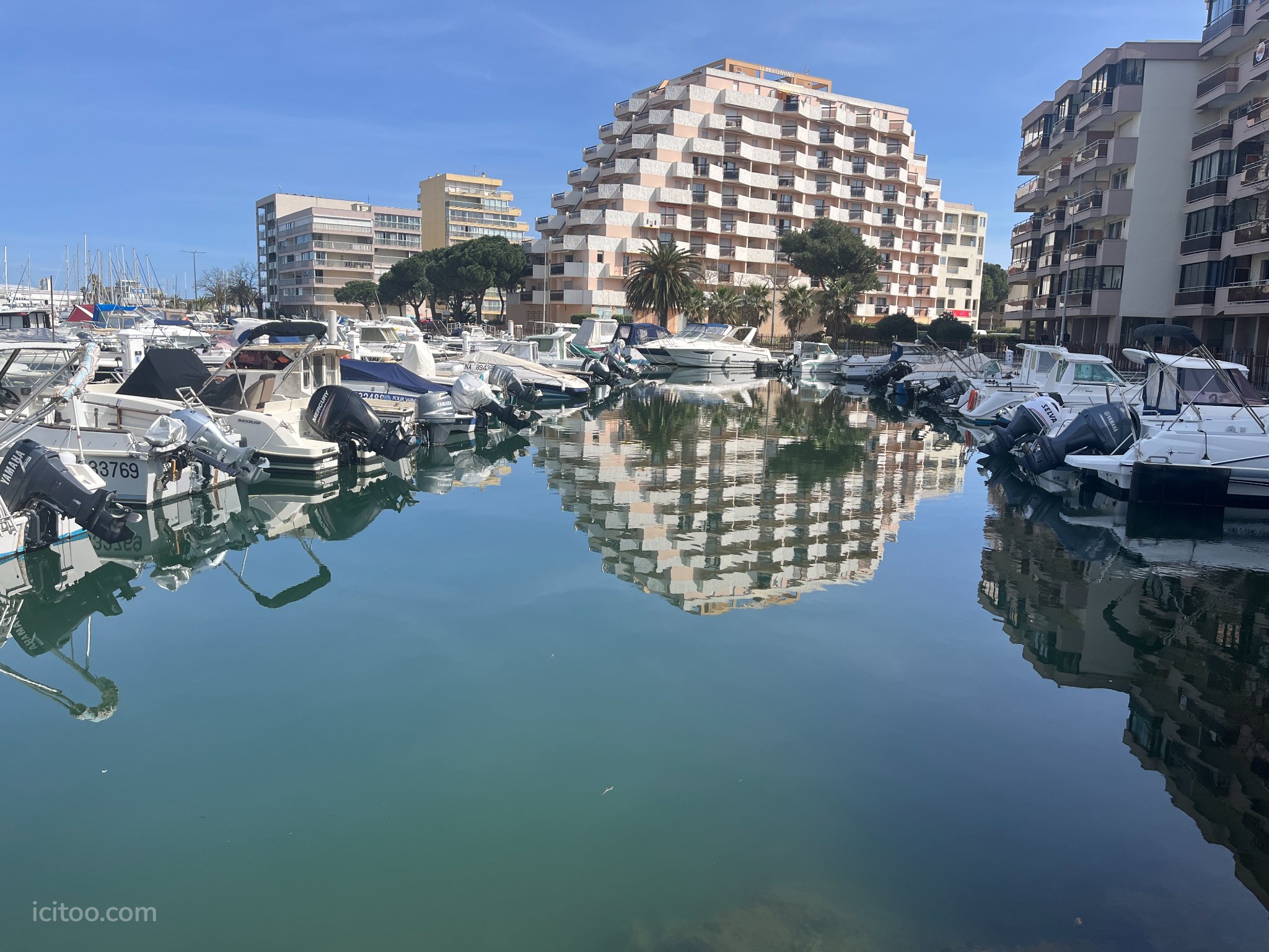 Local commercial à vendre à Canet-en-Roussillon : bâtiments résidentiels et bateaux se reflétant dans l'eau calme