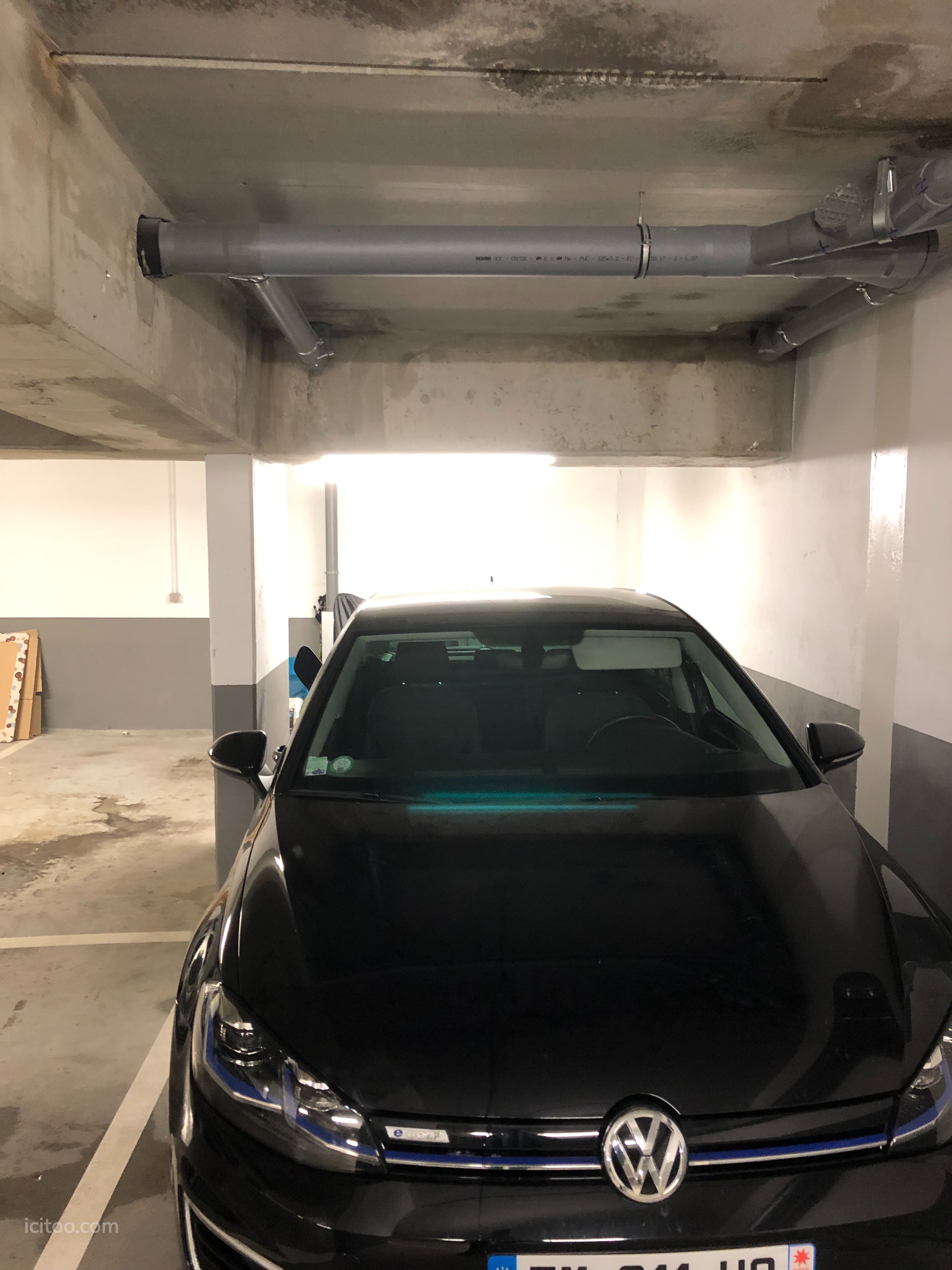 Garage à vendre à Bougival : voiture noire stationnée dans un garage souterrain avec tuyaux apparents
