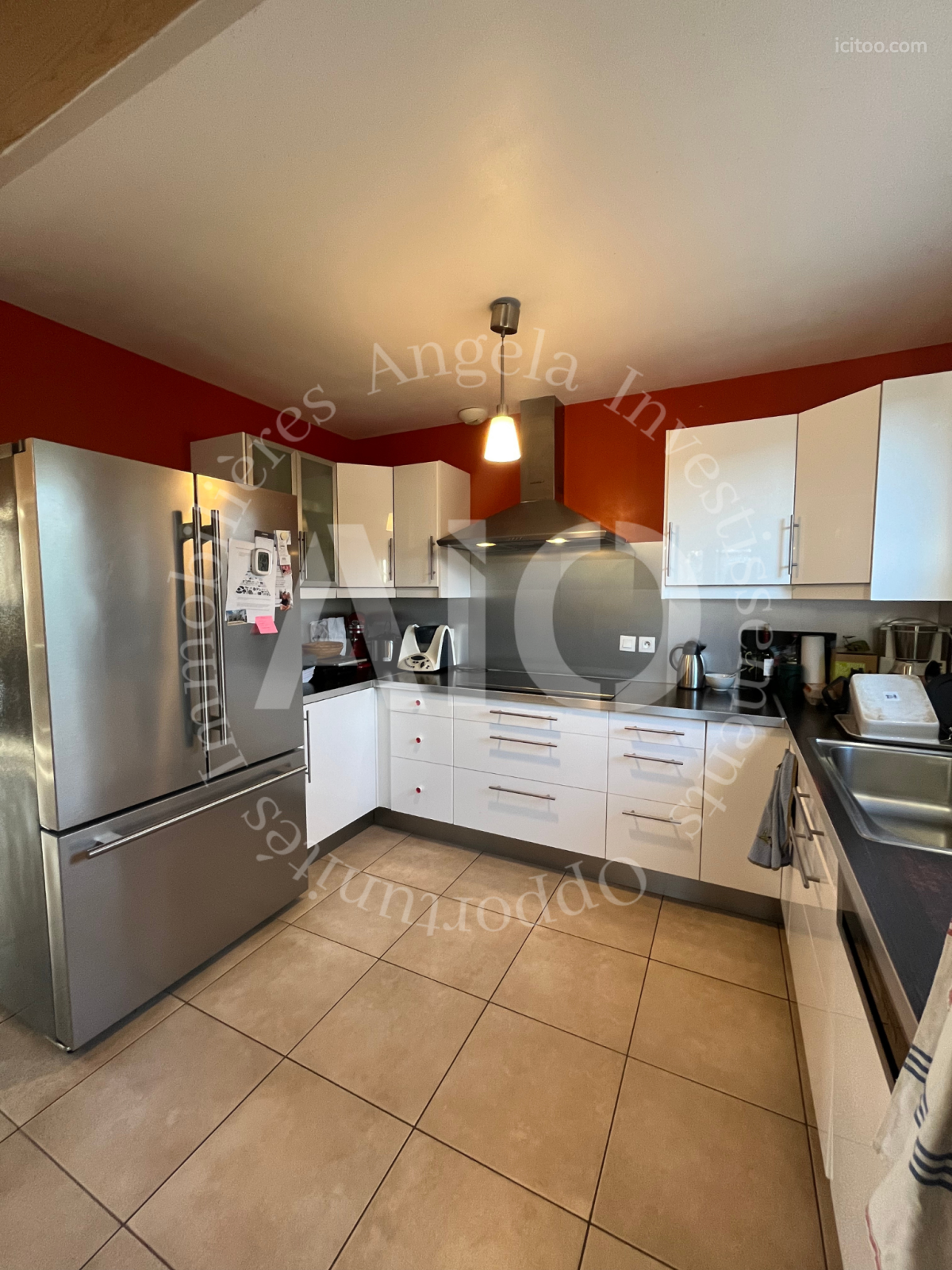 Maison à vendre à Neyron : cuisine avec meubles blancs, plan de travail noir et réfrigérateur inox